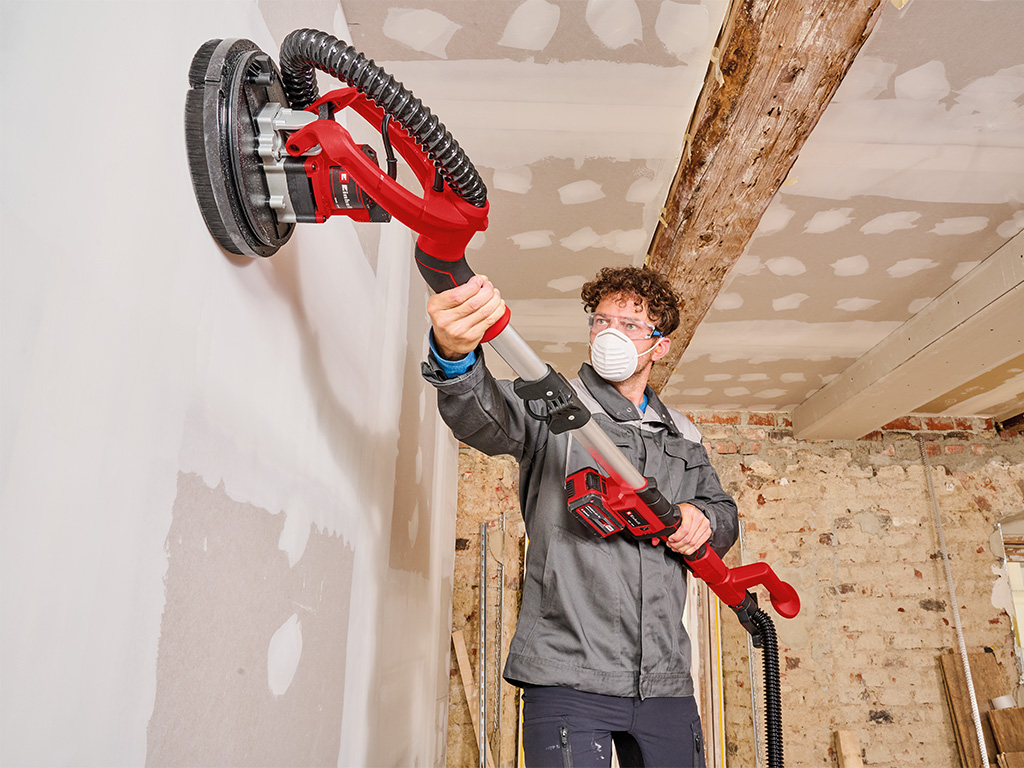 Man with cordless drywall sander sanding drywall at construction site