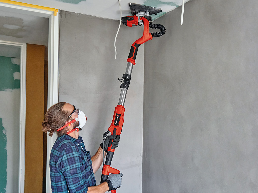 Man with drywall sander sanding a drywall ceiling in the corner of a room