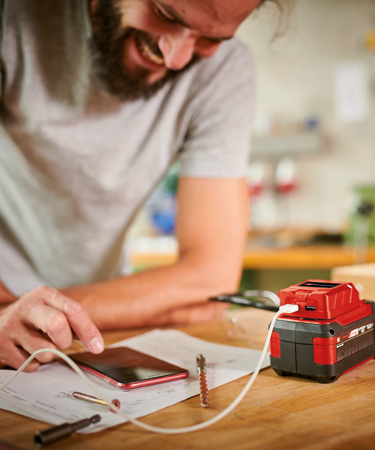 A man charges his phone with the Einhell battery and an USB-Cable