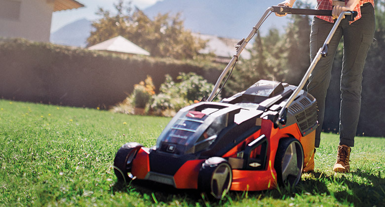 a woman mows the lawn with a lawn mower